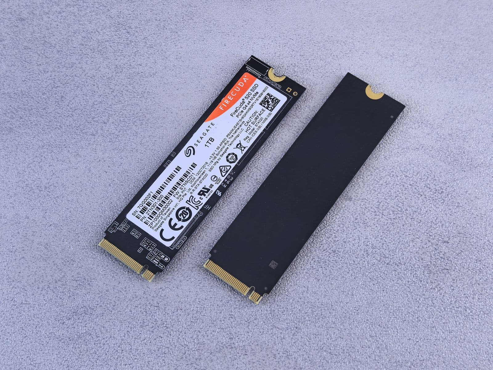 Two M.2 NVMe solid state drives on a grey surface, one showing its label and one its reverse side