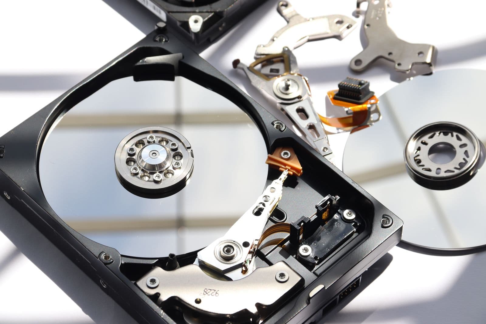 Opened 3.5-inch hard drive showing its platter and read arm, with removed drive parts beside it