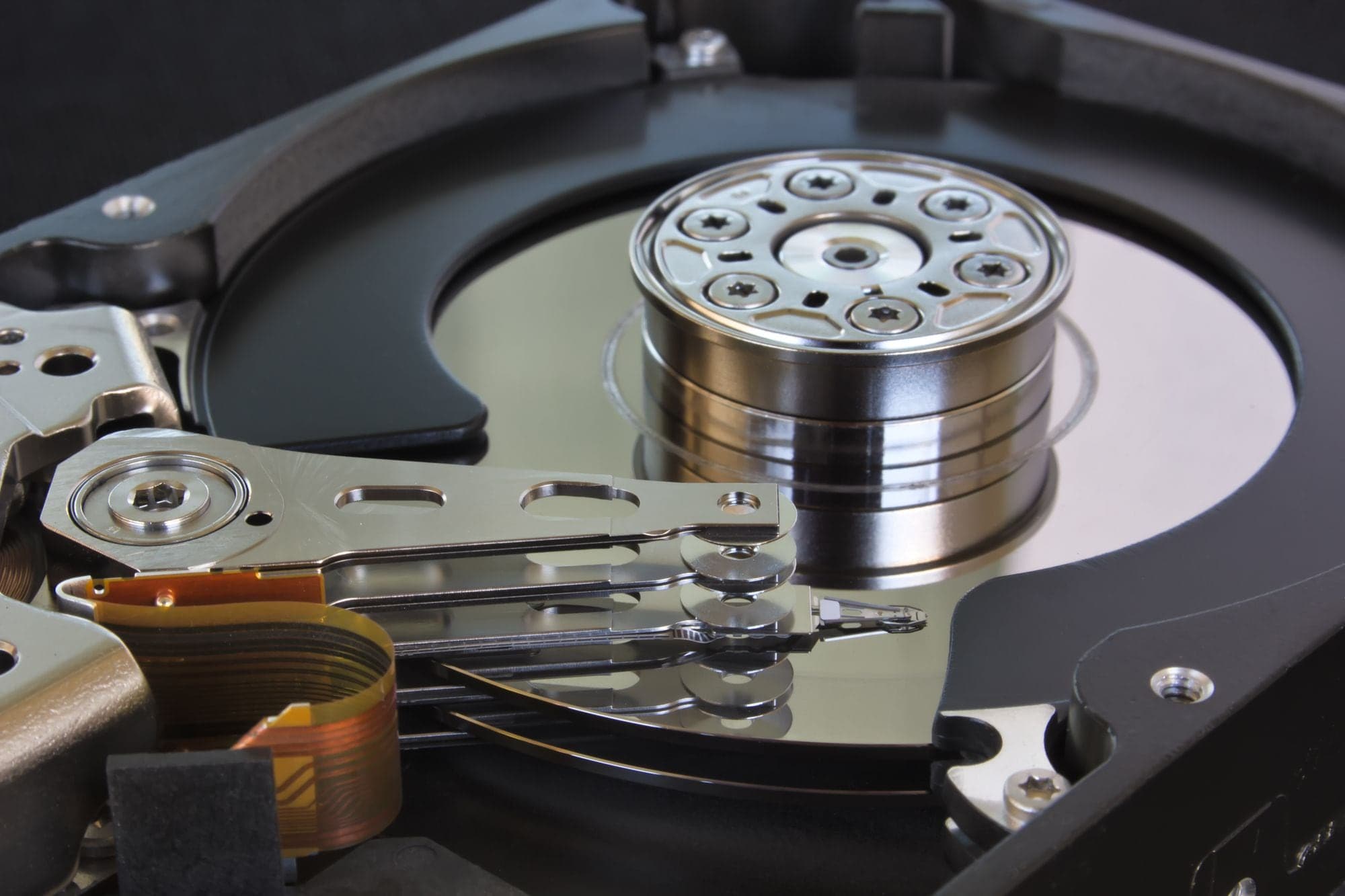 Close-up of an opened hard disk drive showing the spindle hub, platter, read arms and a copper ribbon cable